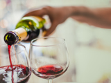 A hand pouring red wine from a bottle into a stemmed glass 