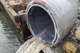 Stormwater flowing from an outfall pipe with a backflow prevention device fitted.