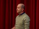 Man standing in front of red curtain giving a speech