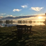 A park bench overlooking an estuary with the sun setting in the background