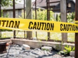 Black and yellow caution tape wrapped around a gateway with rubble on the ground in the foreground